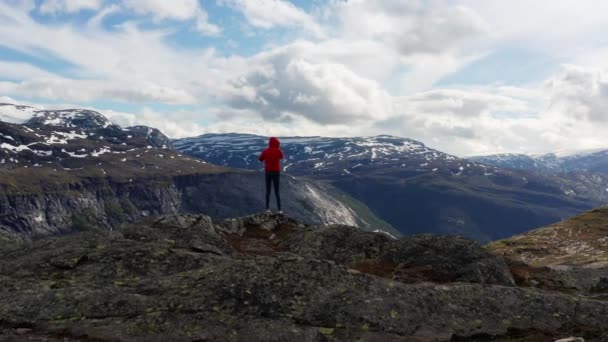 Вид туриста, стоящего на краю скалы в красной куртке — стоковое видео
