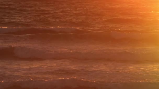 Panning Shot of a Sunset Lit Ocean com ondas rolando com um pico do pôr do sol — Vídeo de Stock