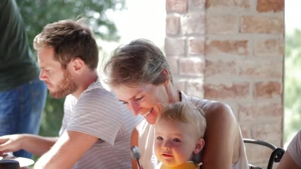 Alte Dame hält ein Kind, während sie mit jemandem beim Familienessen spricht — Stockvideo