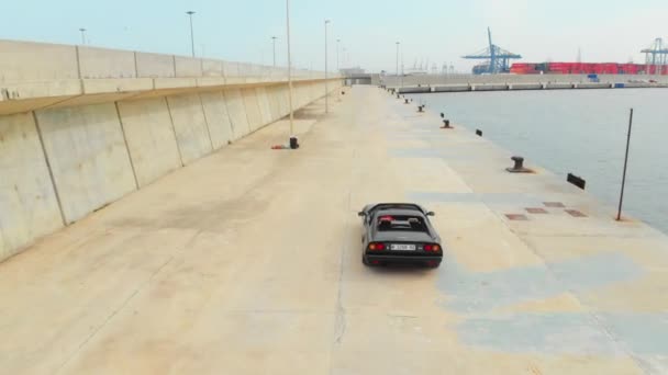 Following Aerial Shot of Man Driving Black Ferrari by the Docks — Stockvideo