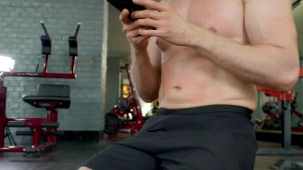 Εστιασμένη Shot of Man Toned Abs καθώς χρησιμοποιεί το τηλέφωνό του ανάμεσα σε ασκήσεις γυμναστικής — Αρχείο Βίντεο