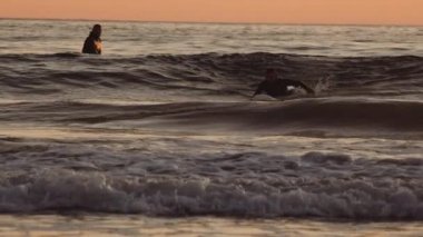 Gün batımında sörfçüler oturur ve tahtada dururlar.