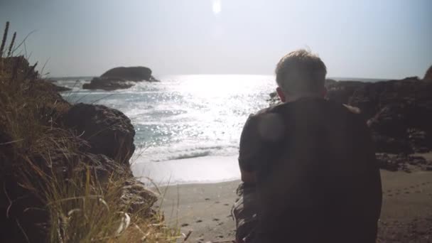 Mann sitzt auf Bresche und blickt aufs Meer — Stockvideo