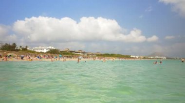 Güneşli bir günde Suda Yüzen ve Sahilde Yürüyen Turist Manzarası