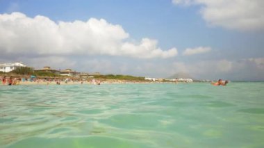 Plajdan uzaklaşırken sörf tahtasına binen bir baba ve oğulun geniş açılı çekimi.