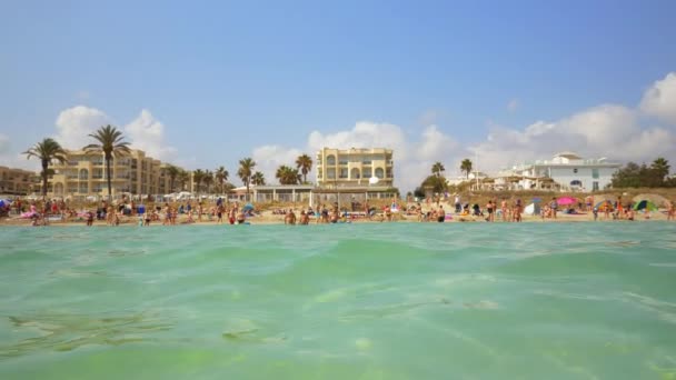 Wide Shot of a Hotel by the Beach con el turista disfrutando del agua en un día soleado — Vídeo de stock