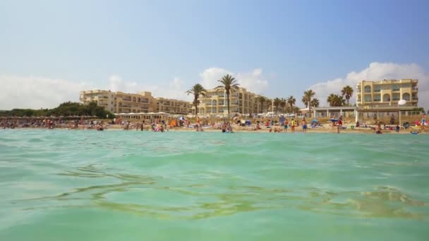 Punto de vista de una cámara flotando en el agua con una vista de los turistas en la playa — Vídeo de stock