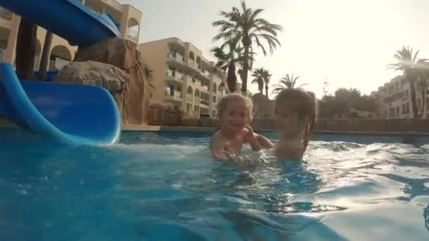 Vidám lány megpróbál elkapni egy fiatalabb fiút, miközben csúszik le a medencén — Stock videók
