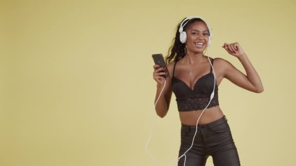 Молодая черная девушка танцует под смартфон и наушники — стоковое видео
