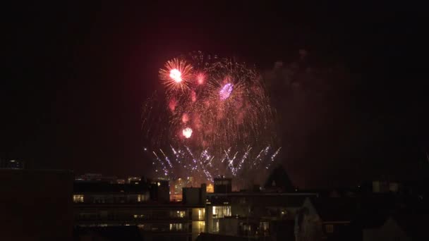 Fuegos artificiales que explotan sobre los tejados de la ciudad en el cielo nocturno — Vídeos de Stock