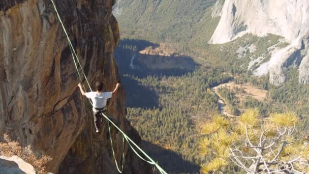 Man met wit shirt probeert op te staan op de slacklining touw en een prachtig uitzicht op de Yosemite Park — Stockvideo