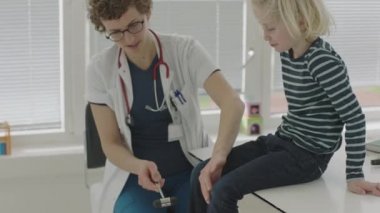 Doktorun, çocuğun diz reflekslerini, refleks olarak çekiçle test ettiği orta boy el kamerası görüntüsü.