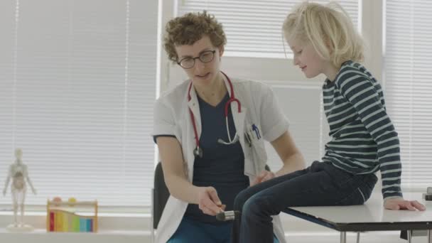 医師の診察で反射ハンマーで少年の膝の反射をスローモーションミディアムハンドヘルドショット — ストック動画