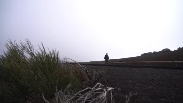 Man loopt langs weg onder bewolkte hemel — Stockvideo