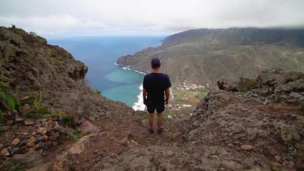 Hombre en la montaña mirando la costa y el mar — Vídeo de stock