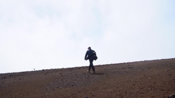 Человек, идущий по каменистой земле к облакам — стоковое видео