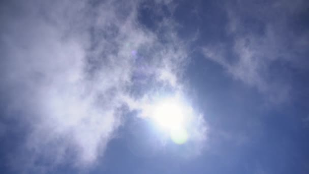 Ljus sol framväxande från moln i blå himmel — Stockvideo