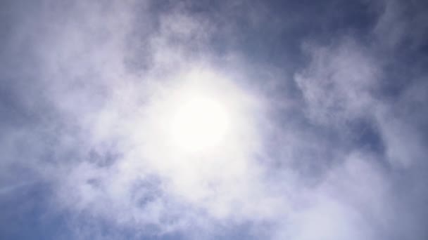 Ljus sol framväxande från moln i blå himmel — Stockvideo