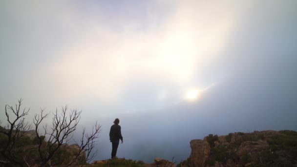 Человек, стоящий на краю скалы и наблюдающий за солнцем — стоковое видео