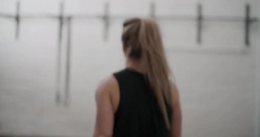 Siyah yelekli bayan sporcu spor salonunda yürüyor.