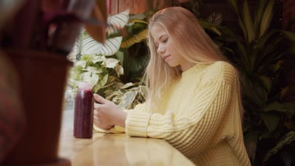 Девушка-блондинка смотрит на телефон в кафе — стоковое видео