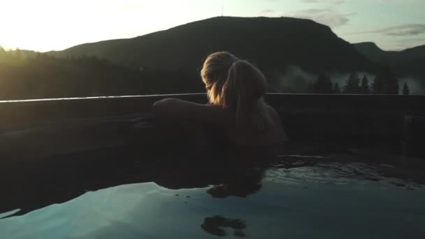 Egy nő lazít a forró fürdőben és nézi a naplementét — Stock videók