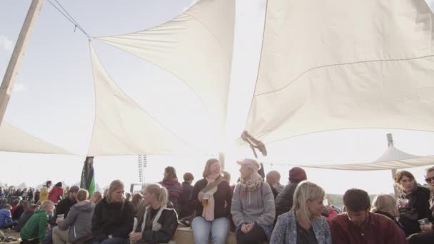 Grande foule de personnes réunies sous une tente blanche avec des reflets du soleil en arrière-plan — Video