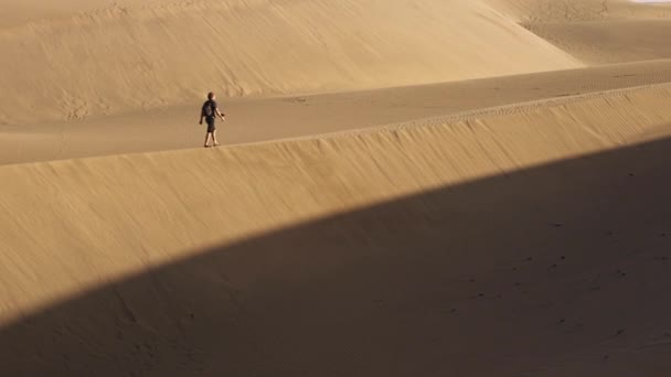 Homme marchant le long de la dune de sable éclairée par le soleil — Video