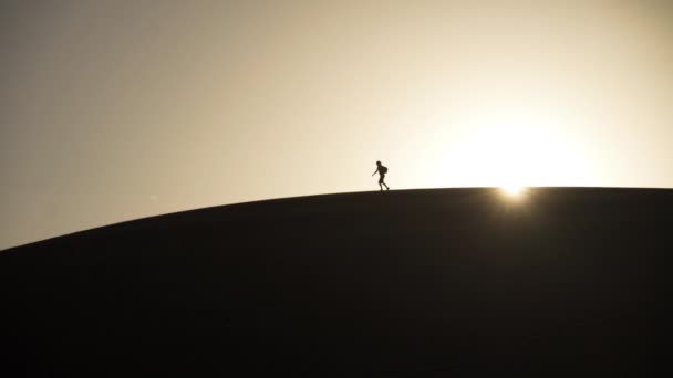 Homem caminhando ao longo da duna de areia iluminada pelo sol — Vídeo de Stock