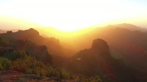 Hombre parado en las rocas mientras el sol se pone sobre las montañas — Vídeos de Stock