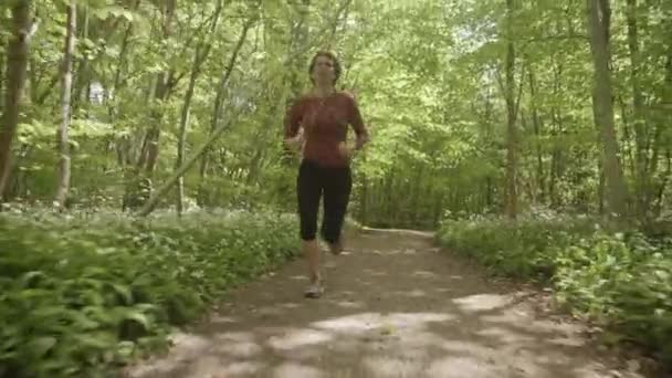 Une femme qui court sur le sentier forestier vers la caméra 