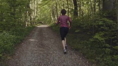 Formda ve sağlıklı kıvırcık saçlı bir kadın ormanda sabah koşusu yapıyor.