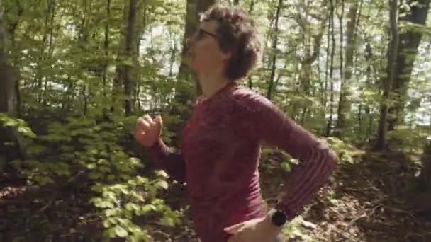 Mujer decidida con gafas corriendo por el sendero del bosque temprano en la mañana — Vídeos de Stock