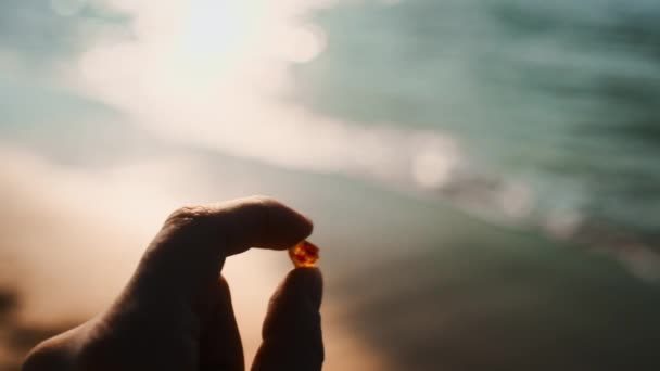 海岸に向かって美しい琥珀を持つ女の手のショット — ストック動画
