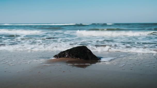 Tiros de uma grande rocha enterrada na costa sendo lavada pelas ondas — Vídeo de Stock