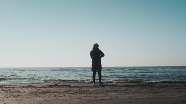 美しい夕日の中海岸を歩く女性のショット. — ストック動画