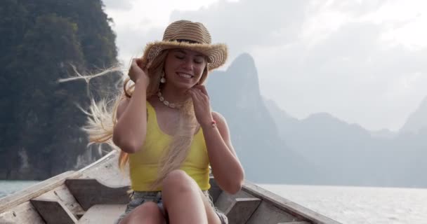 Женщина, держащая Соломенную Шляпу в ветреный день во время прогулки на лодке через озеро — стоковое видео