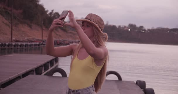 Blond vrouwelijk model Holding Smartphone Up Het nemen van foto van het landschap door Lake — Stockvideo