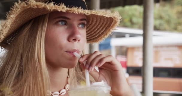 Close-up shot van blonde vrouw in stro hoedje nippen van een rietje — Stockvideo