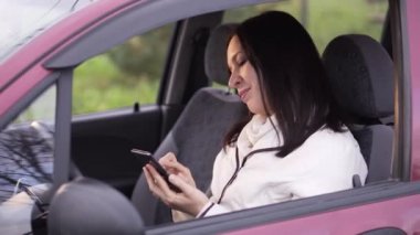 Kadın arabada oturan bir smartphone cep telefonu ile bir ileti yazar