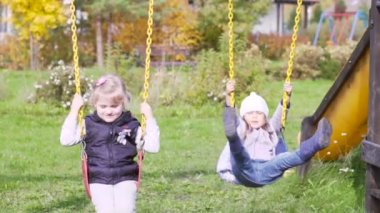 İki güzel küçük kız oyun alanında açık bir salıncak üzerinde