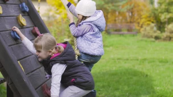 Zwei kleine Mädchen klettern auf dem Spielplatz an der Wand — Stockvideo