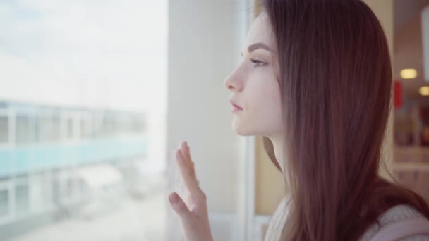 Mujer joven está de pie y mirando por la ventana — Vídeo de stock