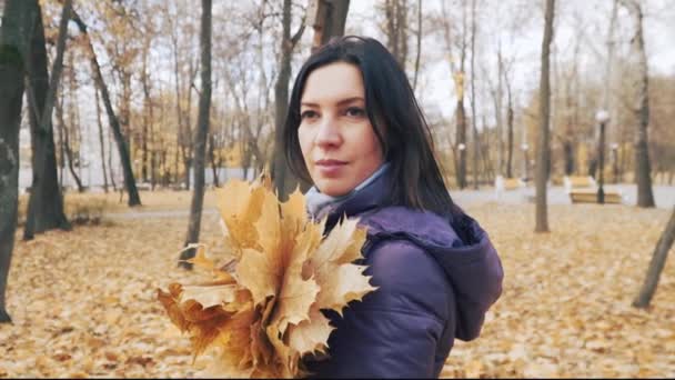Mutlu genç oldukça esmer kadın parkta sonbahar yaprakları buket ile poz. — Stok video