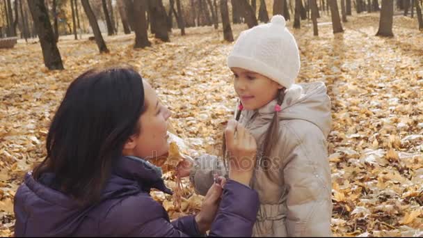 Mãe está aplicando o brilho nos lábios das filhas no parque de outono . — Vídeo de Stock