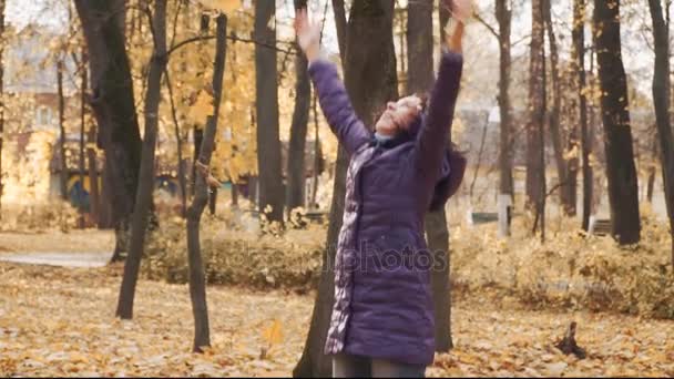 Счастливая молодая красивая брюнетка бросает осенние листья в парке . — стоковое видео
