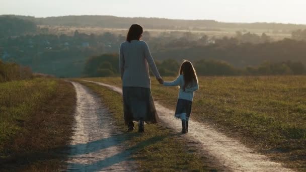 Moeder met dochter wandeling op de landelijke weg in de zonsondergang. — Stockvideo