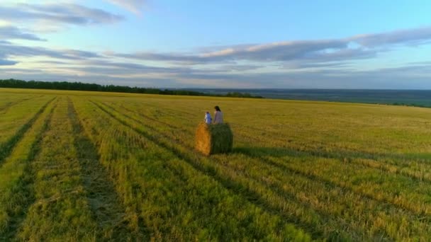 Moeder met dochter zitten op de stro stack op het rustieke veld in de zonsondergang. — Stockvideo