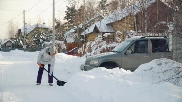 Jovem mulher limpa neve por pá para carro em subúrbios no inverno . — Vídeo de Stock