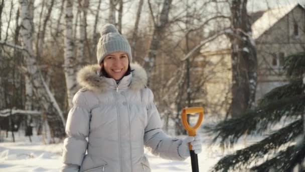 Glückliche junge Frau posiert im Winter mit Schaufel in Vorstädten vor der Kamera. — Stockvideo